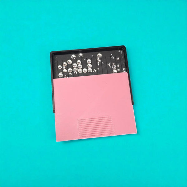 Pink rhinestone tumbler template with clear gems on black tray against teal background