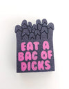 Glittery black pin with pink text saying 'EAT A BAG OF DICKS'