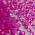 A close-up of many small round pink gemstones or rhinestones scattered on a light surface, with a faint 'The Tumbler Universe' watermark across the center.