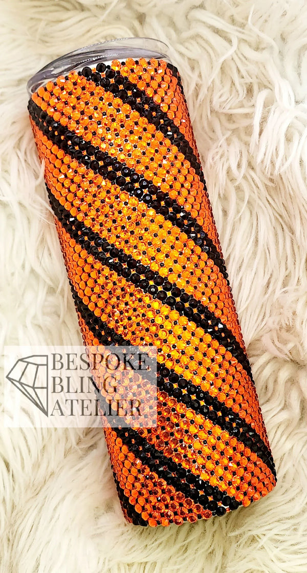 Orange and black rhinestone tumbler with striped bling design on fluffy white background