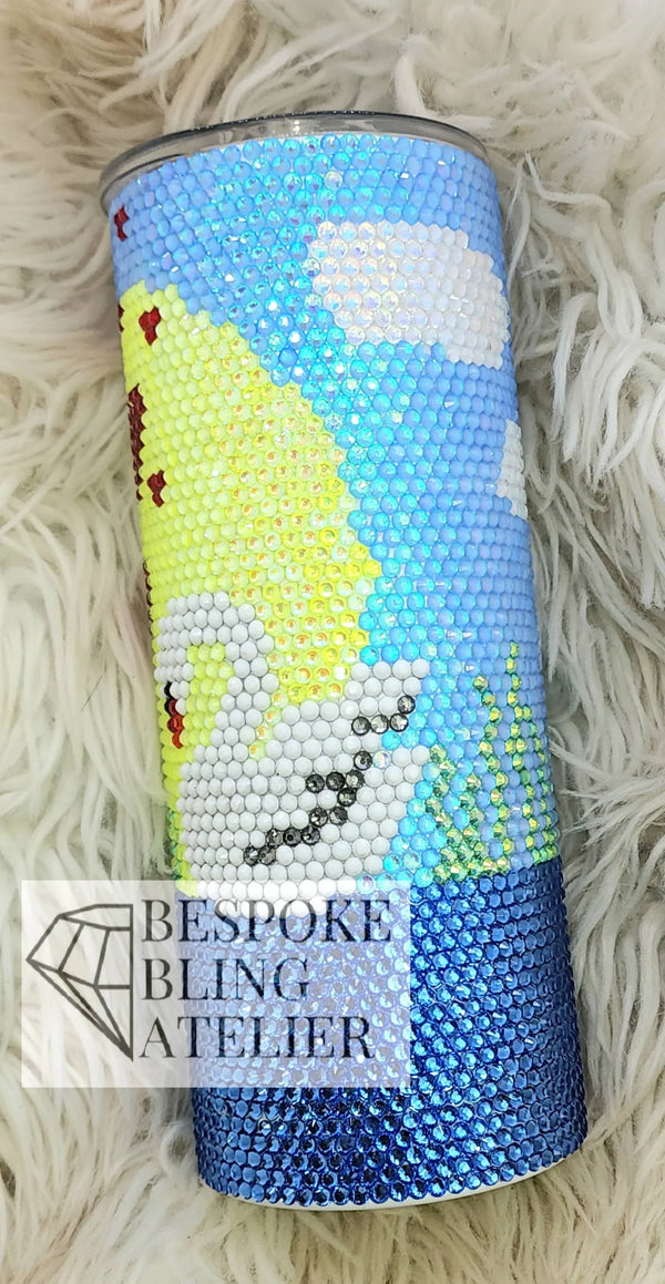Rhinestone tumbler with snowman design, blue sky, and yellow sun on fluffy white background