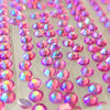A close-up of many round iridescent rhinestones or craft gems on a clear backing sheet, showing pink, purple, and blue reflective colors.