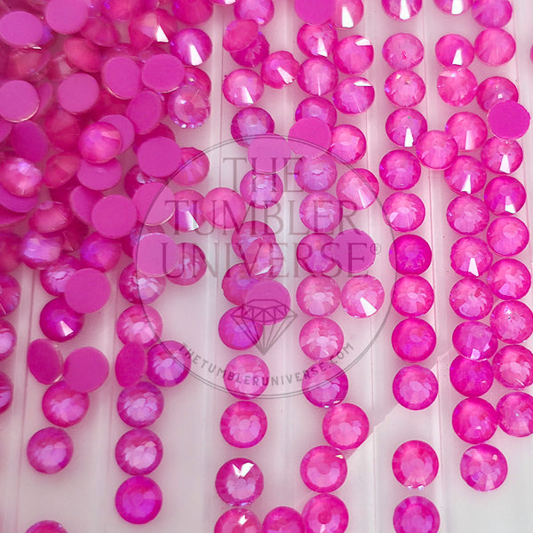 A close-up of many round pink faceted rhinestones or gems scattered across a white surface, with a faint 'The Tumbler Universe' watermark over the center.