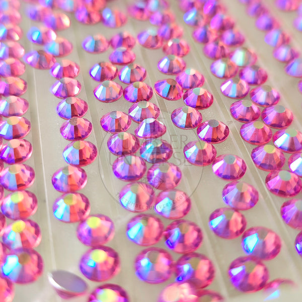 A close-up of many round iridescent rhinestones or craft gems on a clear backing sheet, showing pink, purple, and blue reflective colors.